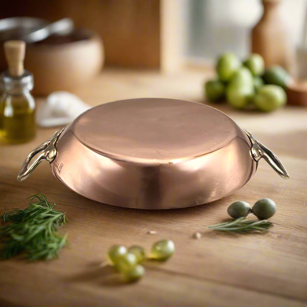 French copper round gratin pan with brass handles on a wooden table with ingredients 
