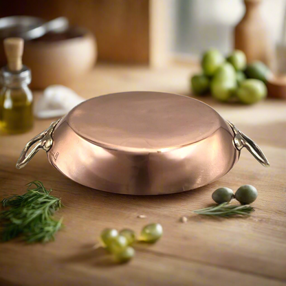 French copper round gratin pan with brass handles on a wooden table with ingredients 