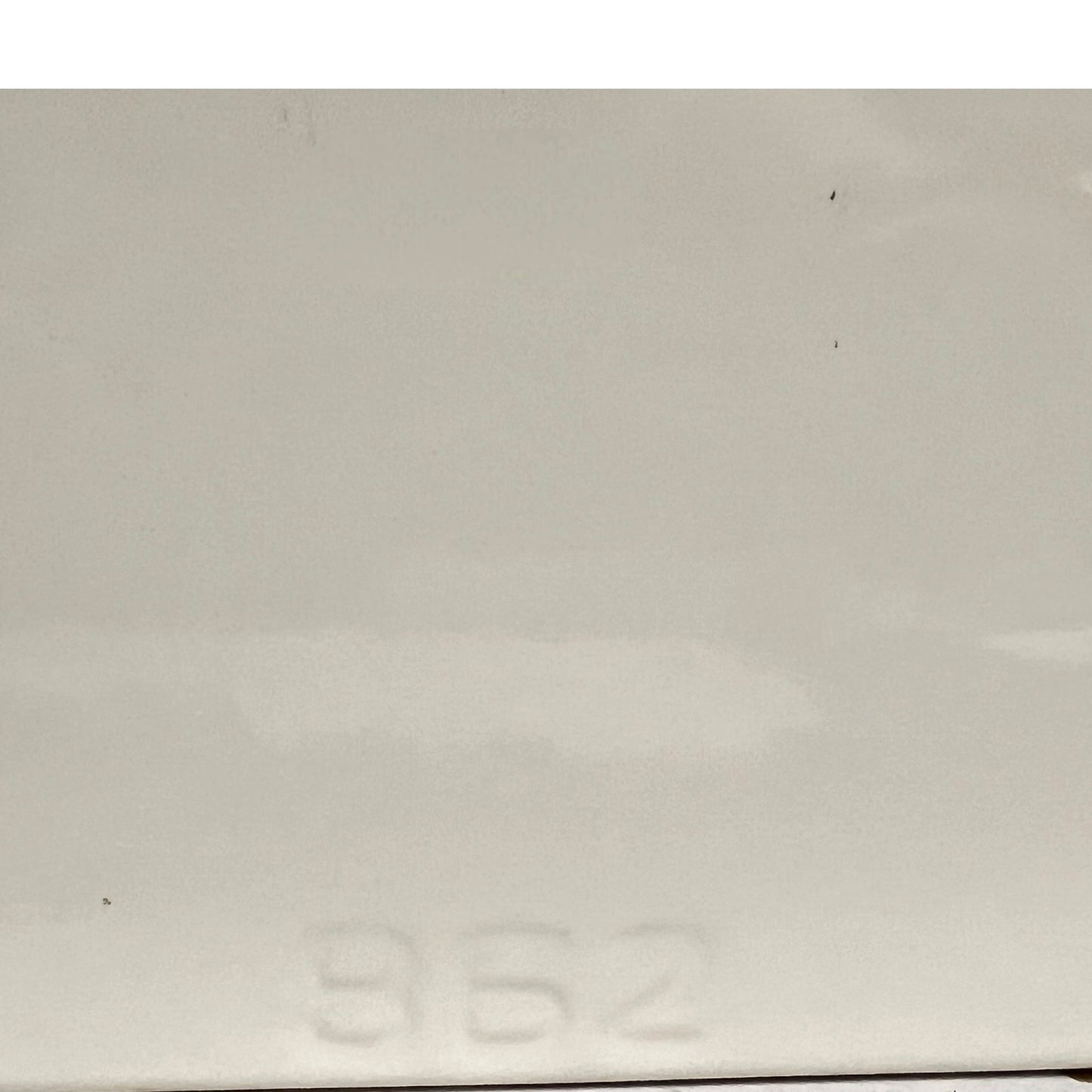 A close-up of a light gray or off-white glossy surface with faint embossed numbers near the bottom and a few small dark specks visible.