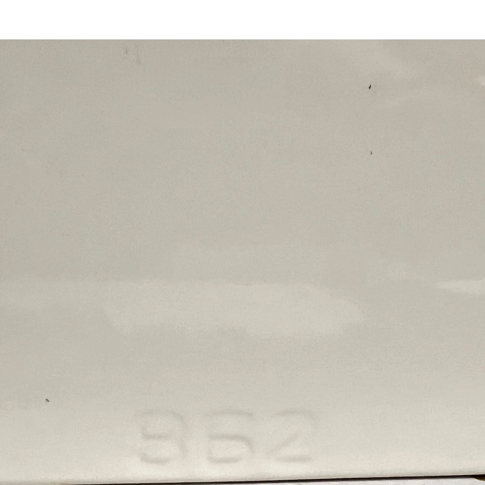 A close-up of a light gray or off-white glossy surface with faint embossed numbers near the bottom and a few small dark specks visible.