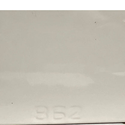 A close-up of a light gray or off-white glossy surface with faint embossed numbers near the bottom and a few small dark specks visible.