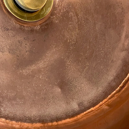 Close-up of a round copper-toned metal surface with a brushed finish and a brass-colored circular detail at the top edge.
