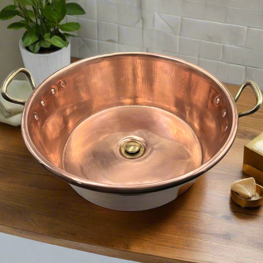 Copper sink on a wooden surface with a plant and decorative items in the background