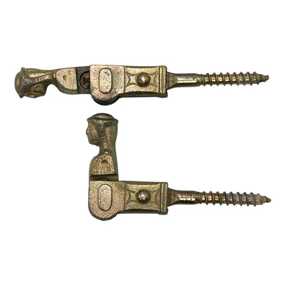 Two brass coloured French decorative shutter brackets on a white background