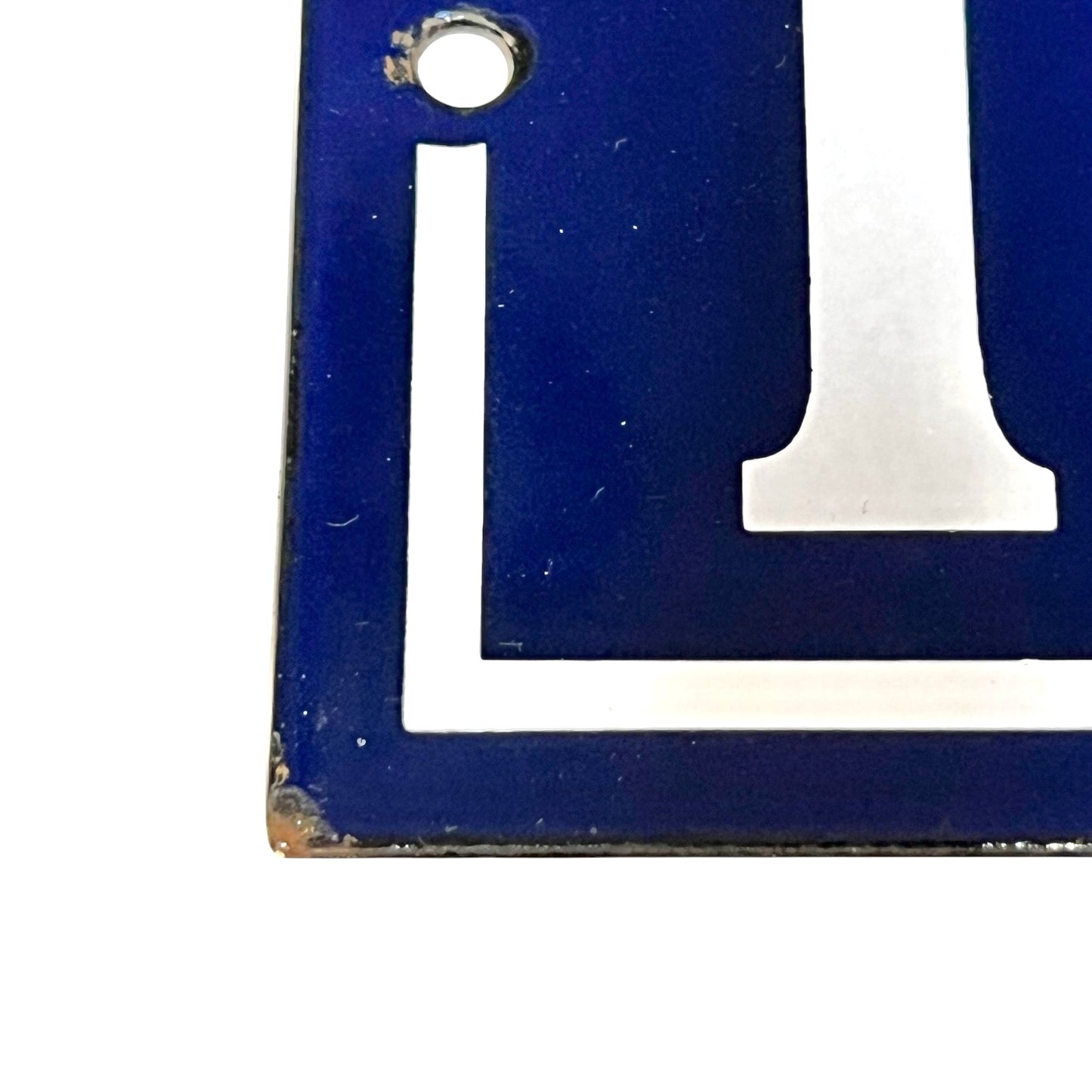 A close-up of a blue enamel numbers with a white border and a small mounting hole, showing some wear and rust on the corner against a white background.