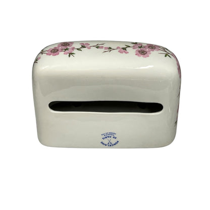 A white ceramic tissue holder with a pink floral pattern along the top edge and a small blue printed logo near the bottom front, shown on a plain white background.