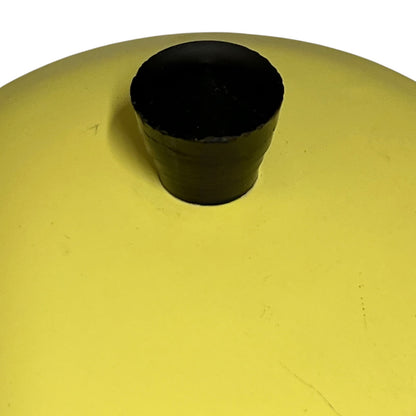 A close-up of a yellow circular surface with a small black cylindrical knob or handle centered on it, photographed against a white background.