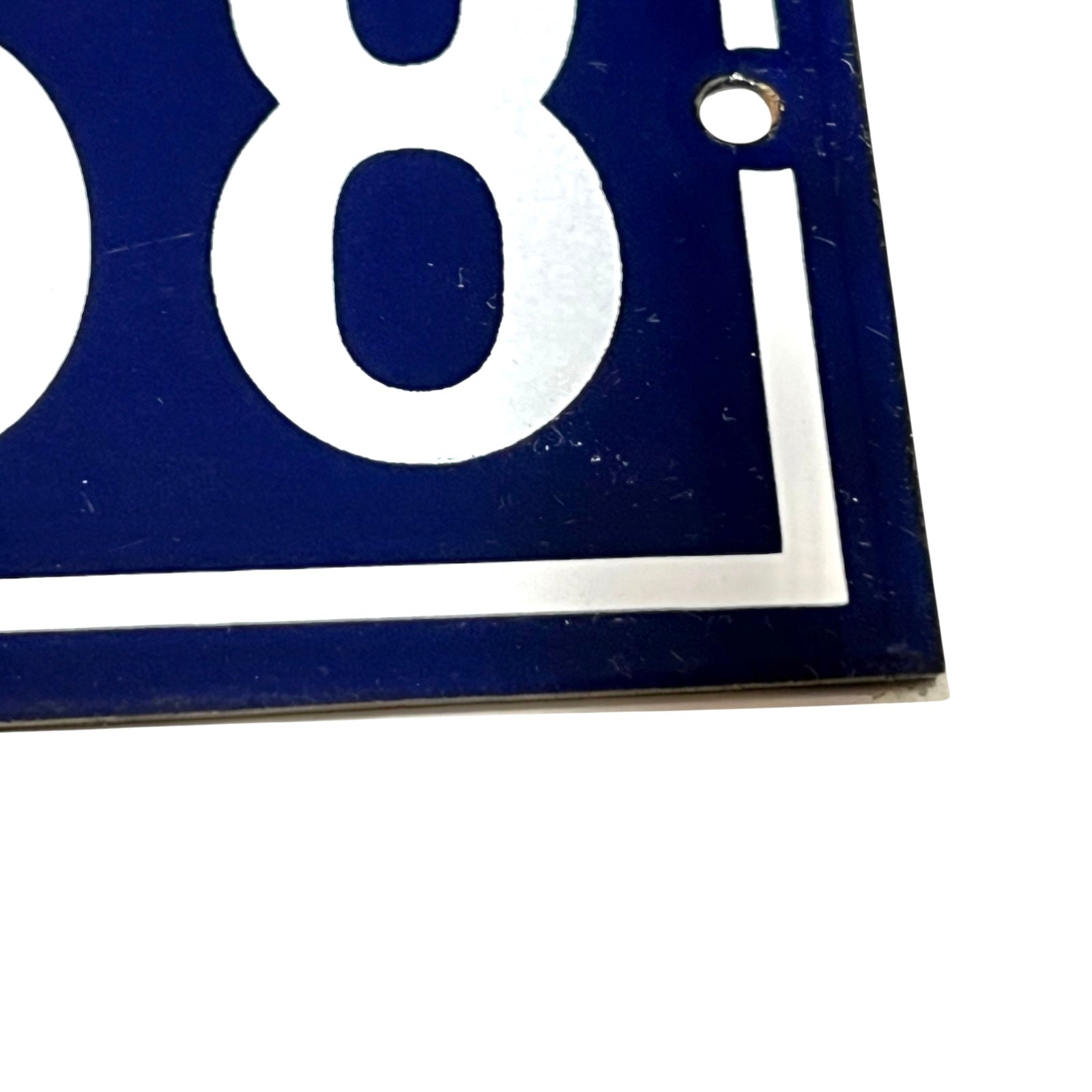 Close-up of a dark blue house number plaque showing the white number 158 and part of the white street-number border, with a mounting hole near the top right.