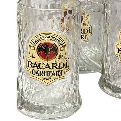 A clear textured glass beer mug with a prominent Bacardi Oakheart logo decal, shown alongside two partially visible identical mugs on a white background.