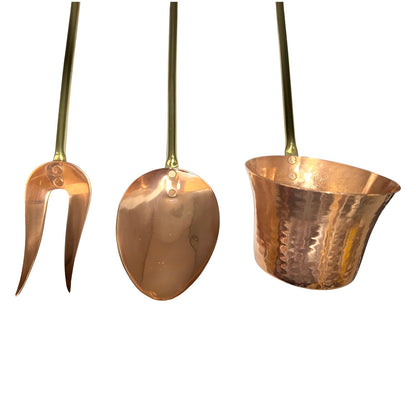 Three copper bar tools with long brass handles, including a two-pronged server, a spoon, and a small cup, shown against a plain white background.