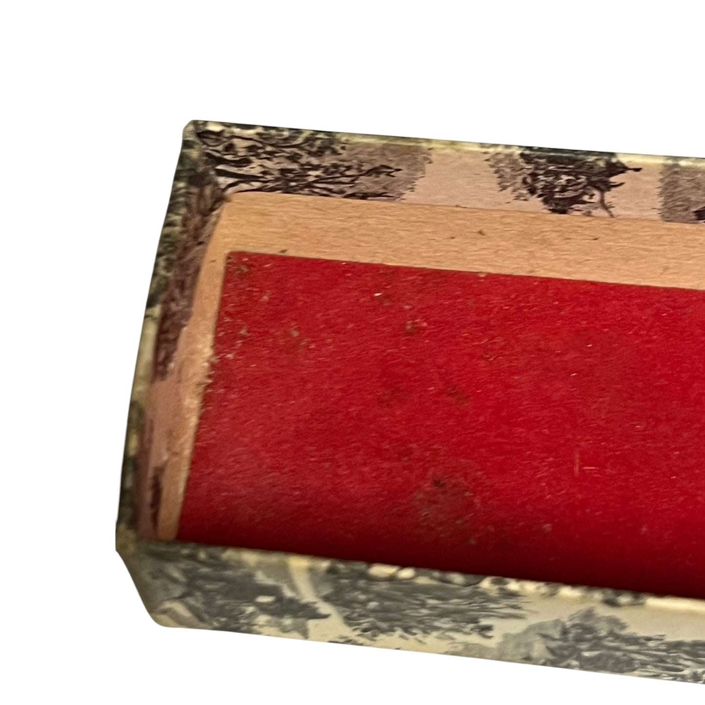 A close-up of a rectangular red velvet cushion or pad set inside a patterned box with a beige and black toile-style print.