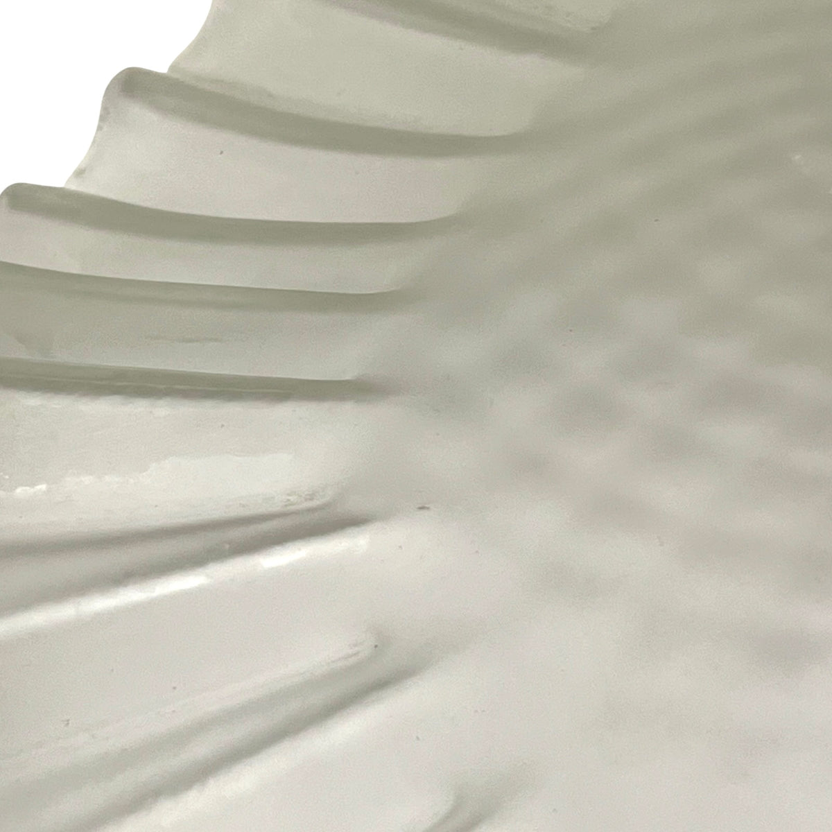 Close-up of a white translucent glass shade with a scalloped rim and a textured, dimpled surface.
