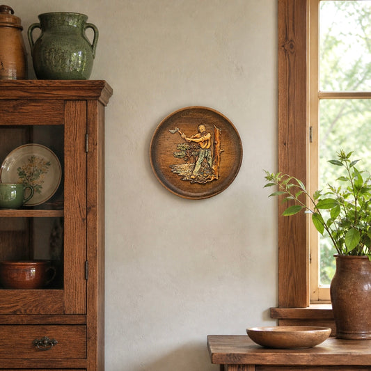 French round vintage wooden wall plaque with a 3d resin/plastic scene in relief of a woodcutter chopping a tree, rustic Arts and Crafts in style, ideal for a country home, set on a wall beside a wooden cabinet in a rustic kitchen with a window and a vase of greenery