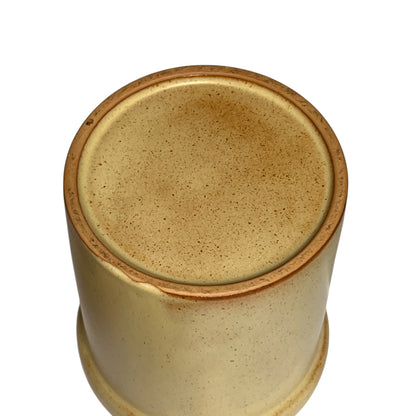 A close-up top-down view of a cylindrical ceramic planter or vase with a speckled beige and light brown glaze, set against a plain white background.