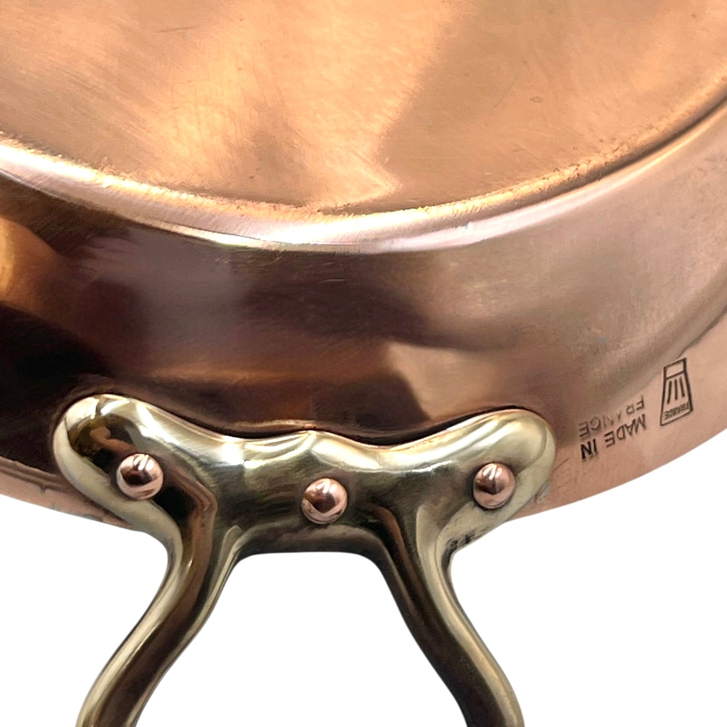 French copper round gratin pan with brass handles showing a chefs hat makers stamp and the words Made in France on a white background