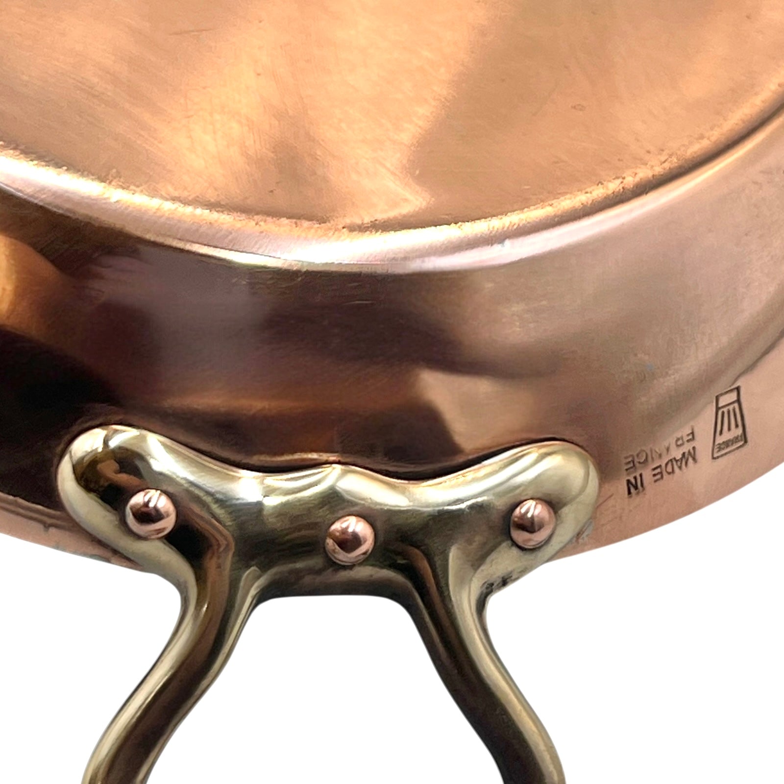 French copper round gratin pan with brass handles showing a chefs hat makers stamp and the words Made in France on a white background
