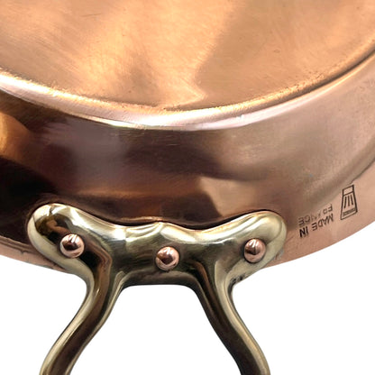 French copper round gratin pan with brass handles showing a chefs hat makers stamp and the words Made in France on a white background