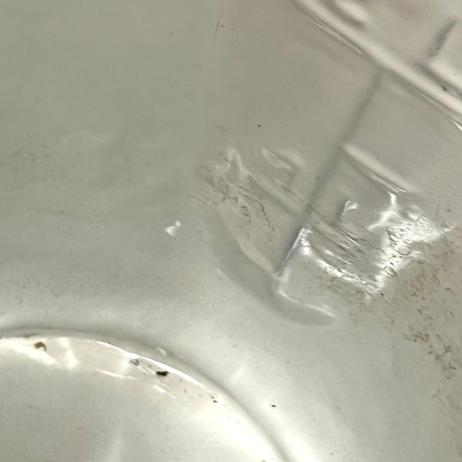 A close-up view of a enamel pot showing a scuffed, scratched, and dirty surface with some dust particles visible.