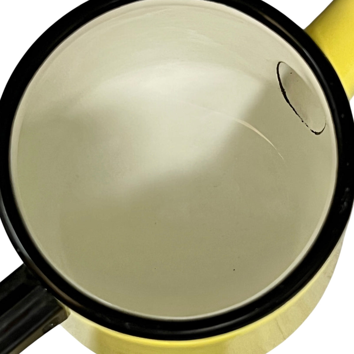Close-up top view of a yellow enamel pot or saucepan with a black rim and black handle, showing the interior surface and a small circular detail near the upper right.