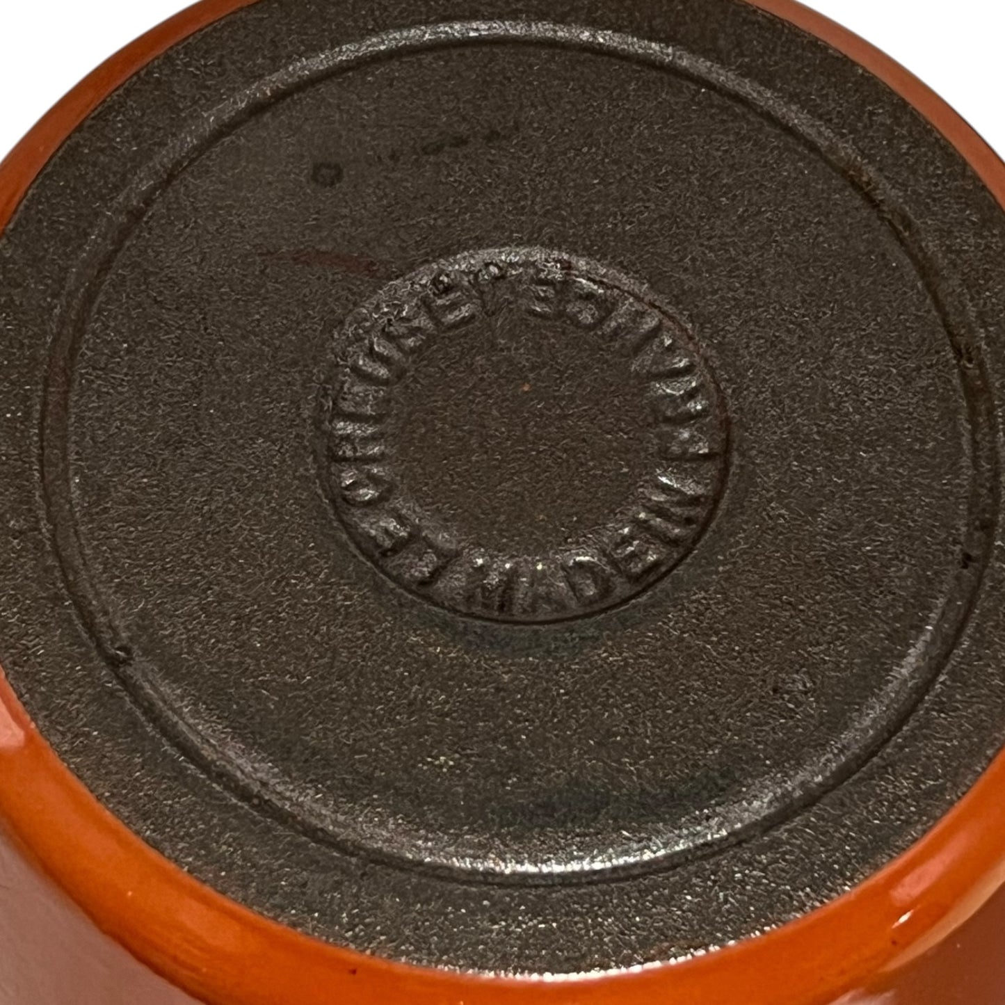 Close up of a rust coloured cast iron saucepan with lid on a white background