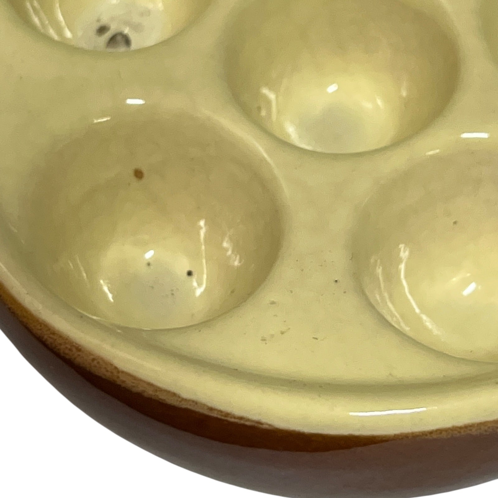 Close-up of a ceramic six-dish snail plate with a glossy cream-coloured glazed interior and a brown unglazed clay rim, shown on a white background.