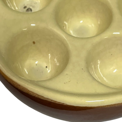Close-up of a ceramic six-dish snail plate with a glossy cream-coloured glazed interior and a brown unglazed clay rim, shown on a white background.