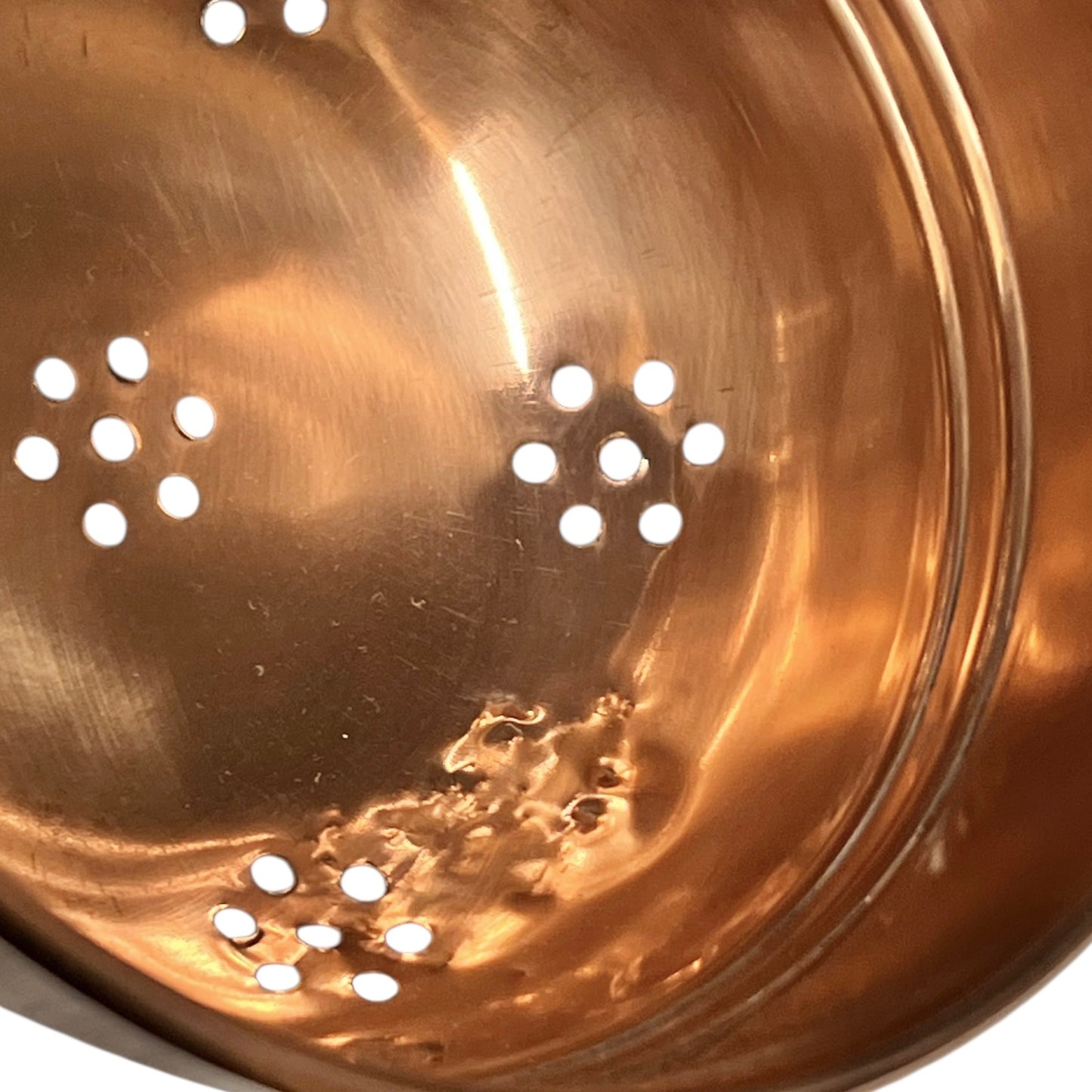 Close-up of a copper strainer with holes on a white background