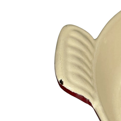 Close-up of a cream-colored cast iron dish with a red rim, shown against a plain white background.