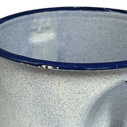Close-up of a speckled blue enamel jug with a dark blue rim, showing a small chip on the edge.