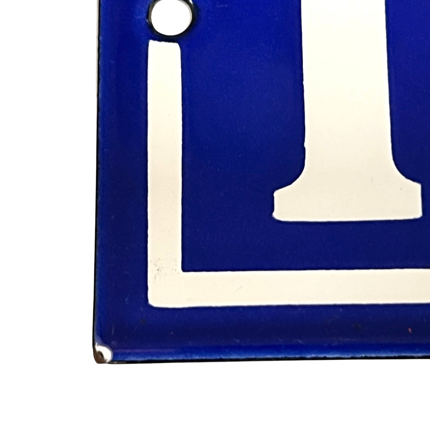 A close-up of a square blue enamel sign with a white painted number and a small mounting hole near the top left corner.