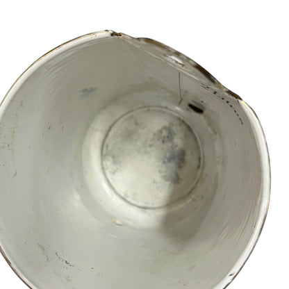 An overhead close-up of a white planter with  a chipped rim, showing some scuffs and dirt inside, on a white background