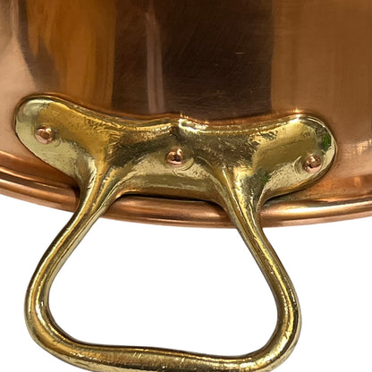Close-up of a polished copper pot with a decorative brass loop handle and rivets on a white background.