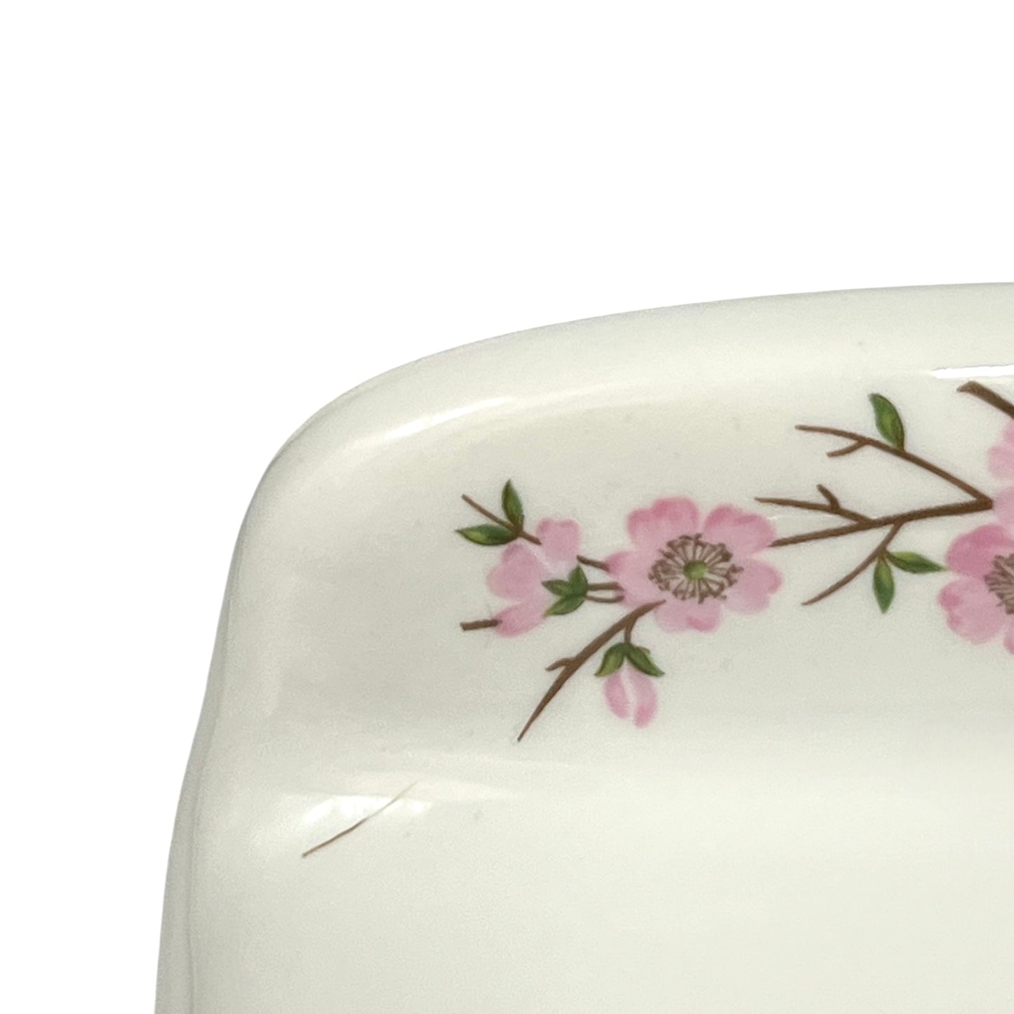 Close-up of a glossy white ceramic plate corner decorated with a delicate pink floral branch pattern on a white background.