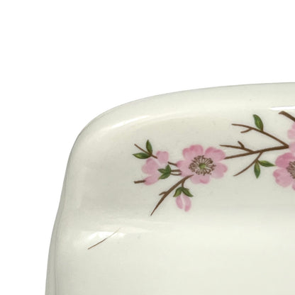 Close-up of a glossy white ceramic plate corner decorated with a delicate pink floral branch pattern on a white background.