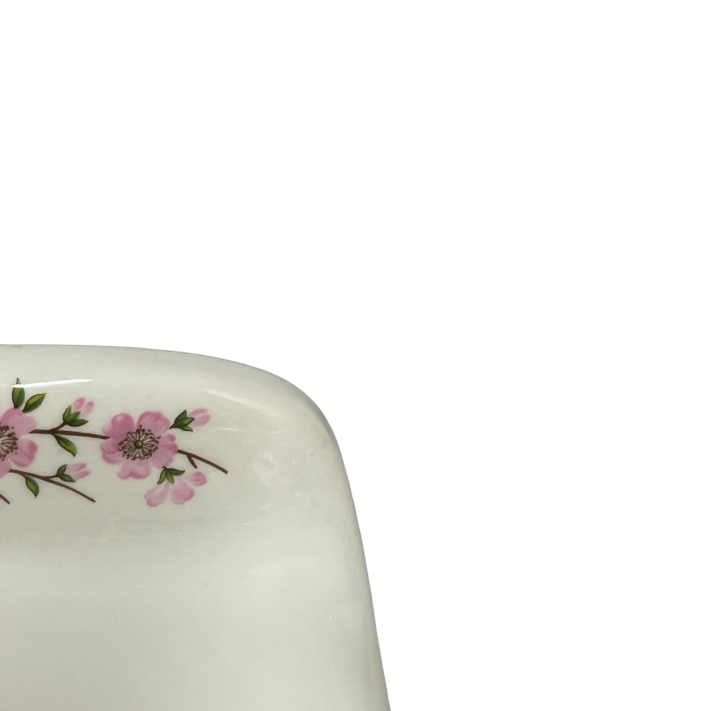 Close-up of the rounded corner of a glossy white ceramic dish or plate decorated with a delicate pink floral branch motif on a plain white background.