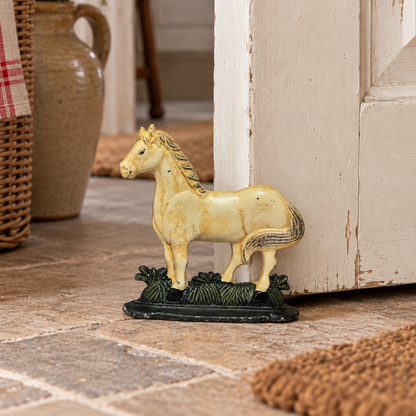 Vintage cast iron horse doorstop with cream painted finish and green base, styled beside a rustic farmhouse door.