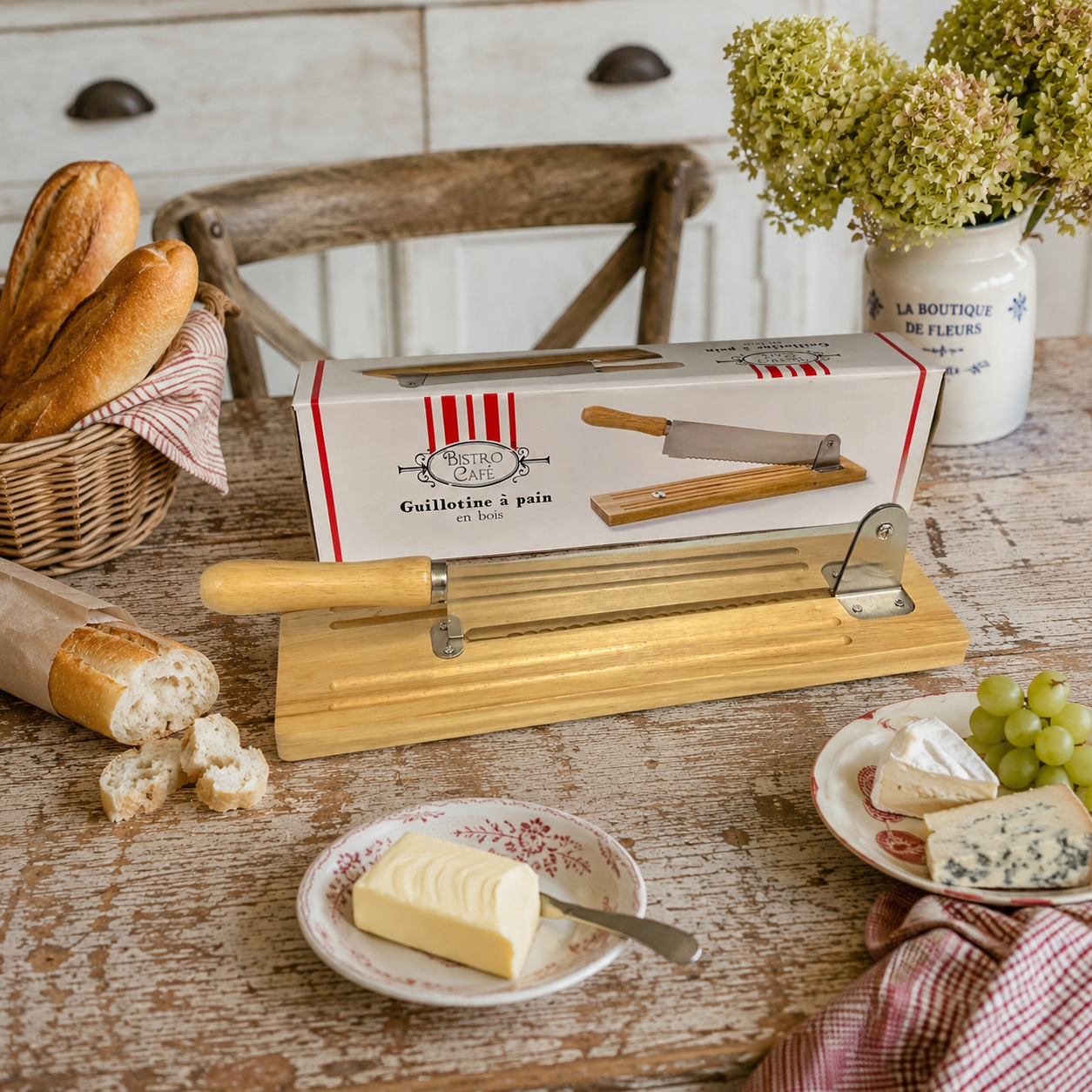 A wooden French bread slicer or baguette cutter, paired with a Bistro Cafe branded box, perfect for adding charm to a farmhouse or country kitchen backdrop - displayed on a French kitchen table alongside a baguette, butter and some cheese