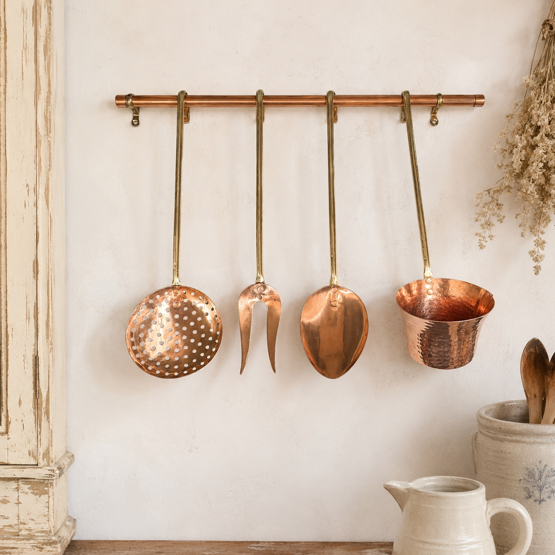 French copper and brass hanging kitchen utensils on a copper rang displayed on a rustic farmhouse wall 