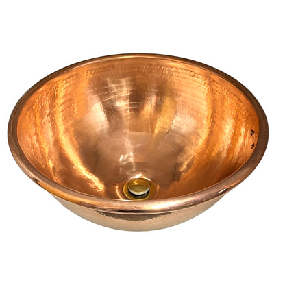 A hammered copper bathroom sink basin with a polished interior and a brass drain, shown on a plain white background.