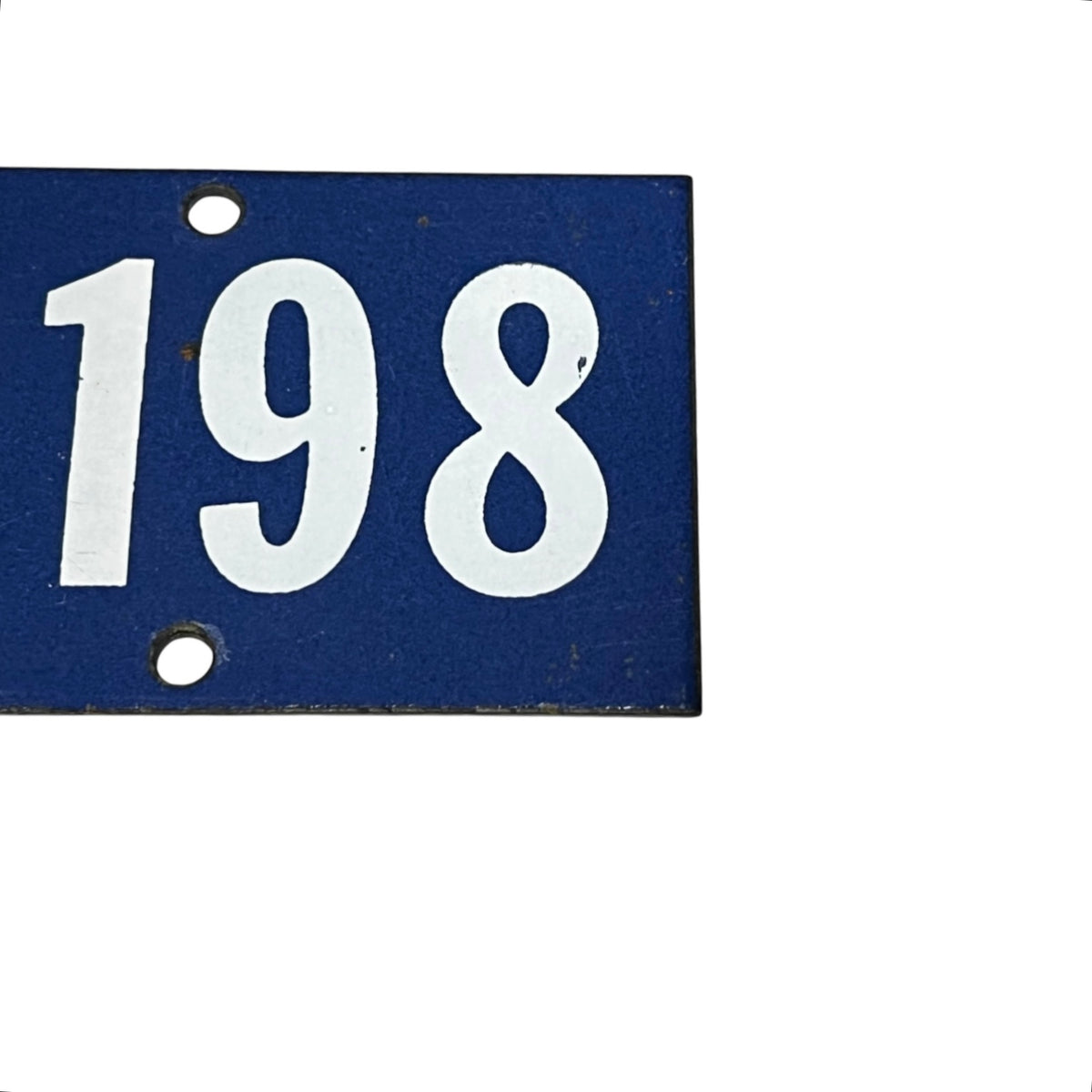 A close-up of a rectangular blue house number plaque showing '198' in white, with two mounting holes, on a plain white background.