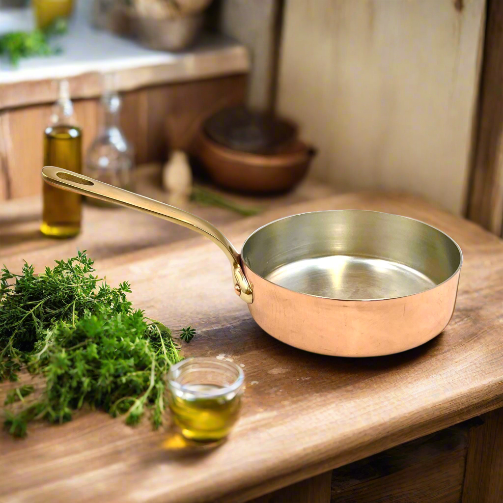 Copper frying pan on a wooden surface with herbs and oil in the background