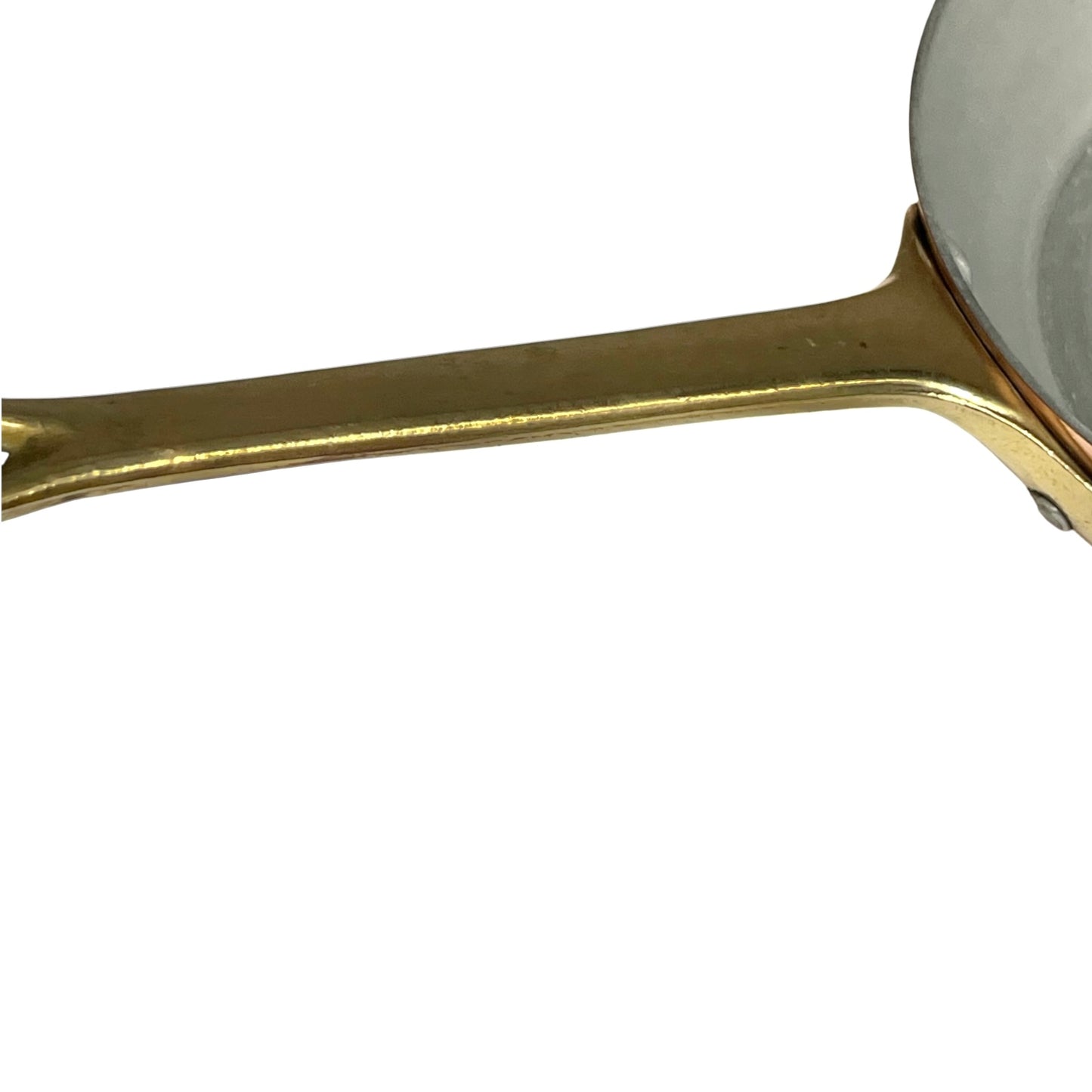 Close-up of a brass handle and part of a copper frying pan on a plain white background.