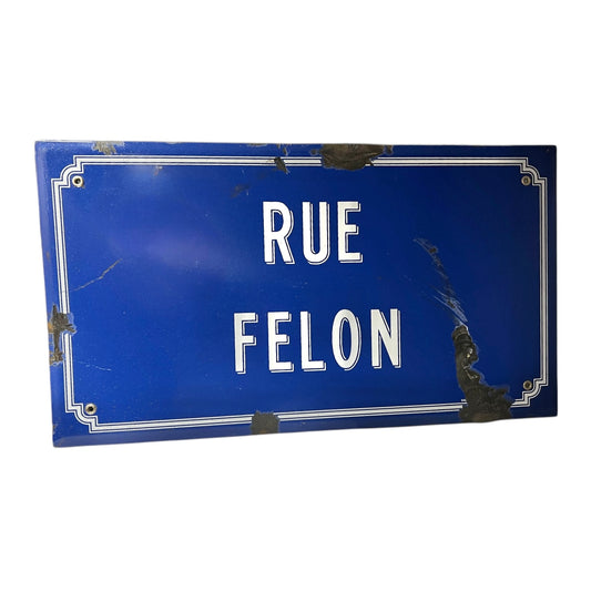 Blue street sign with white text 'RUE FELON' on a white background