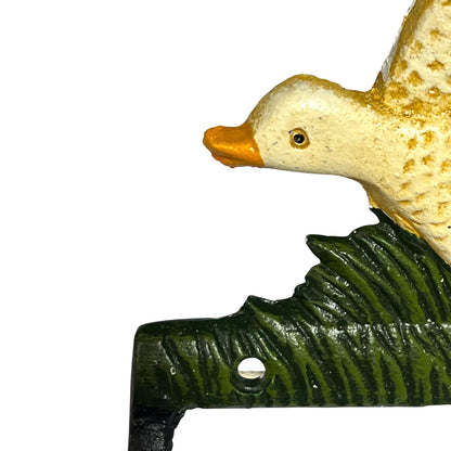 Close-up of a decorative duck figurine perched on a dark green leafy branch, shown against a plain white background.