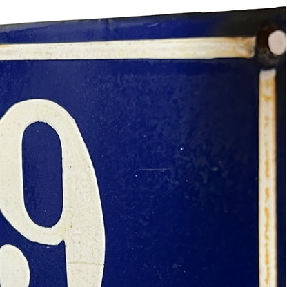 Close-up of a dark blue sign or plaque with a large off-white number 9 and a vertical mounting rod at the right edge.