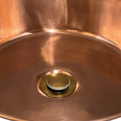 Close-up of a copper sink with a drain and stopper.