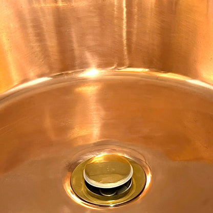 Close-up of a copper sink with a drain plug on a white background