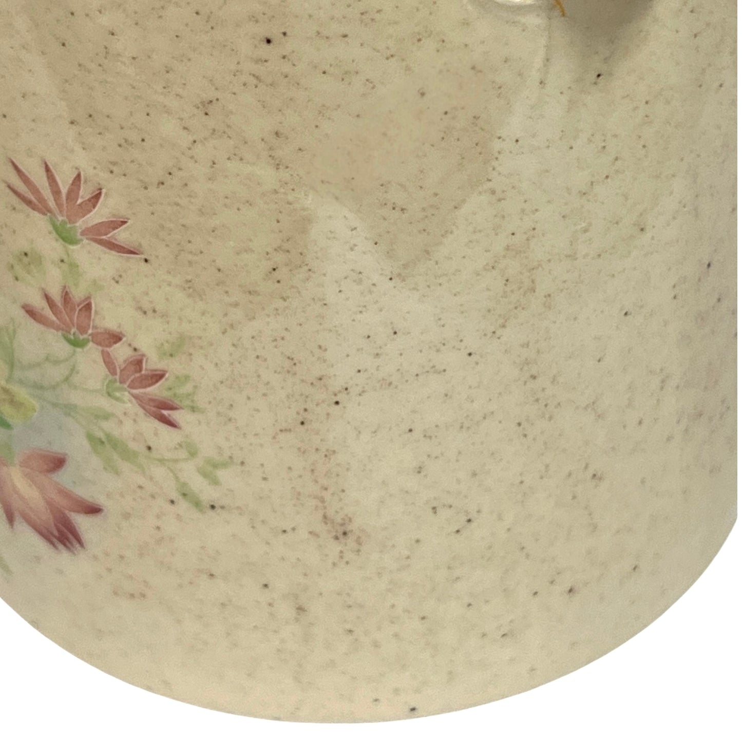 Close-up of a ceramic vessel showing a speckled cream-beige glaze with a painted floral motif in muted pink and green on the left side.