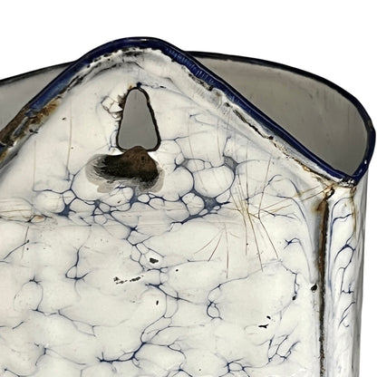 A close-up of a cylinder shaped container or vase with a white and blue crackled pattern, featuring a dark blue rim and a small central hole.