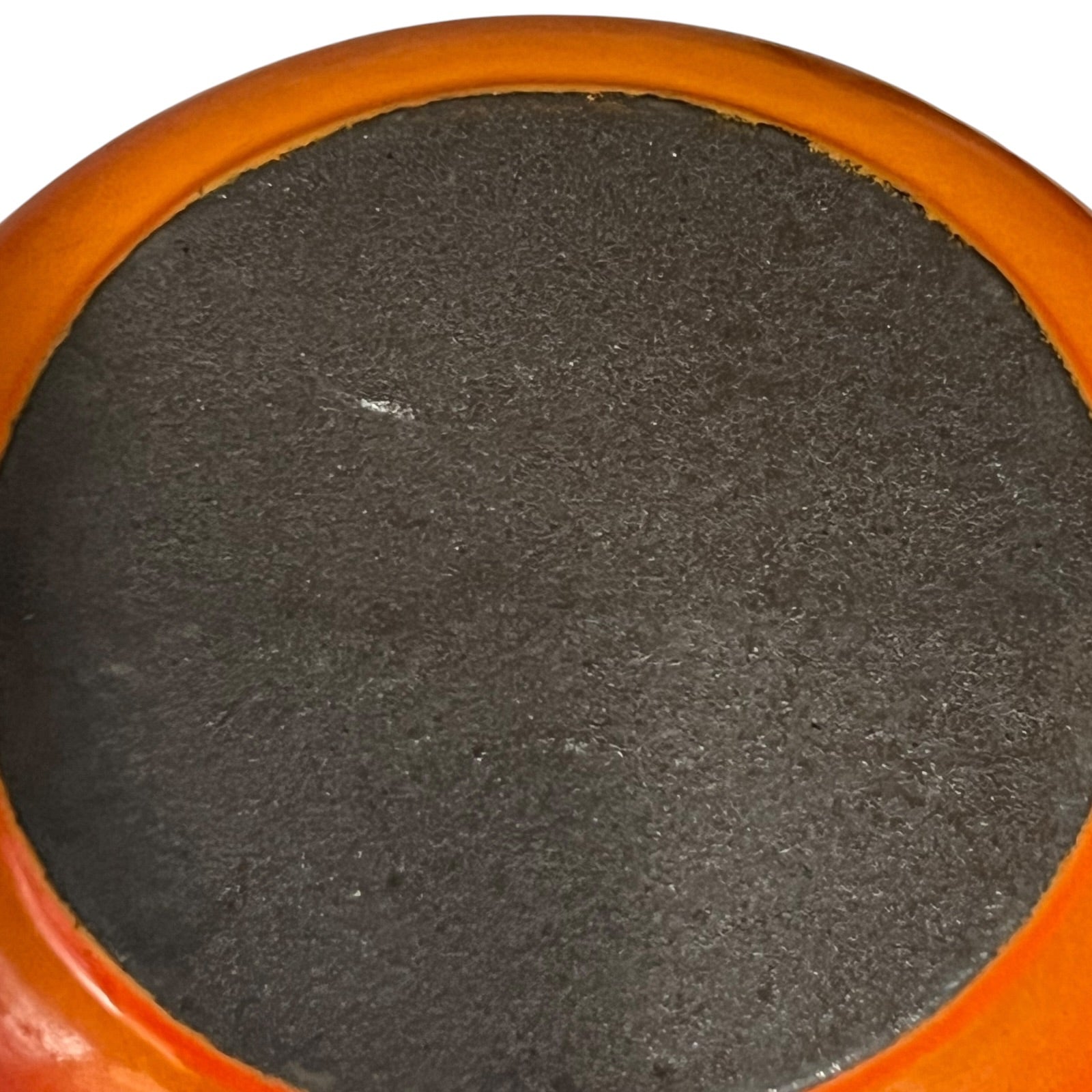 Close-up of a circular dark charcoal or black textured surface with a glossy orange rim, shown against a white background.